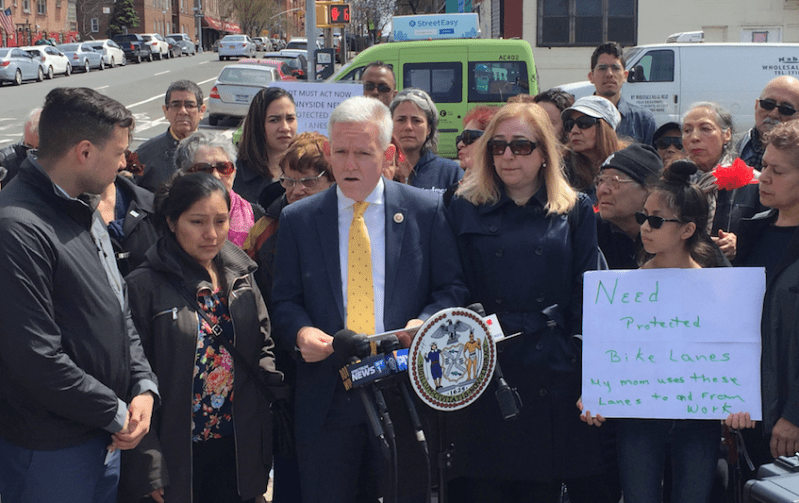 City Council Majority Leader Jimmy Van Bramer, podium, speaking this morning alongside Flor Jimenez, left, whose husband Gelacio Reyes was killed biking on 43rd Avenue on April 1. Photo: David Meyer