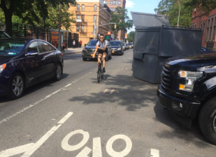 The cars (and dumpster) that intrude into the bike lane by the 88th Precinct aren't going anywhere -- it's the bike markings that are shifting over. Photo: David Meyer