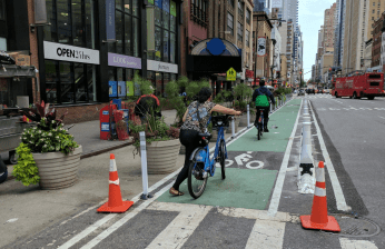 The wider pedestrian zone is separated from the bike lane by planters, and the bike lane is separated from motor vehicle traffic by inexpensive bollards and low-profile barriers. Photo: NYCFreeParking/Twitter