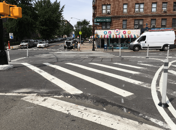 A sidewalk extension, temporarily demarcated with paint and flex posts, provides a shorter, more direct crossing on Broadway at Isham and W. 211th streets, where the A train connects with several bus lines. Photos: Brad Aaron