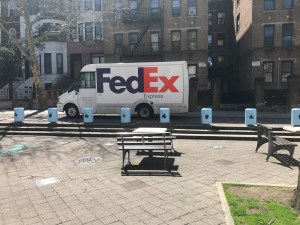 A FedEx truck drives on the sidewalk right next to the park on St. Mark's Avenue.