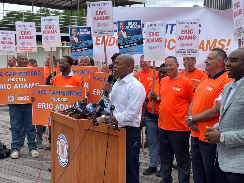 Eric Adams wears a white shirt and stands in front of a group of carpenters in Brooklyn Bridge Park as he receives their endorsement.