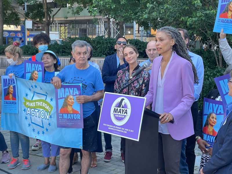 Maya Wiley wears a light blue suit and talks to a group of supporters behind a podium in Hudson Yards.