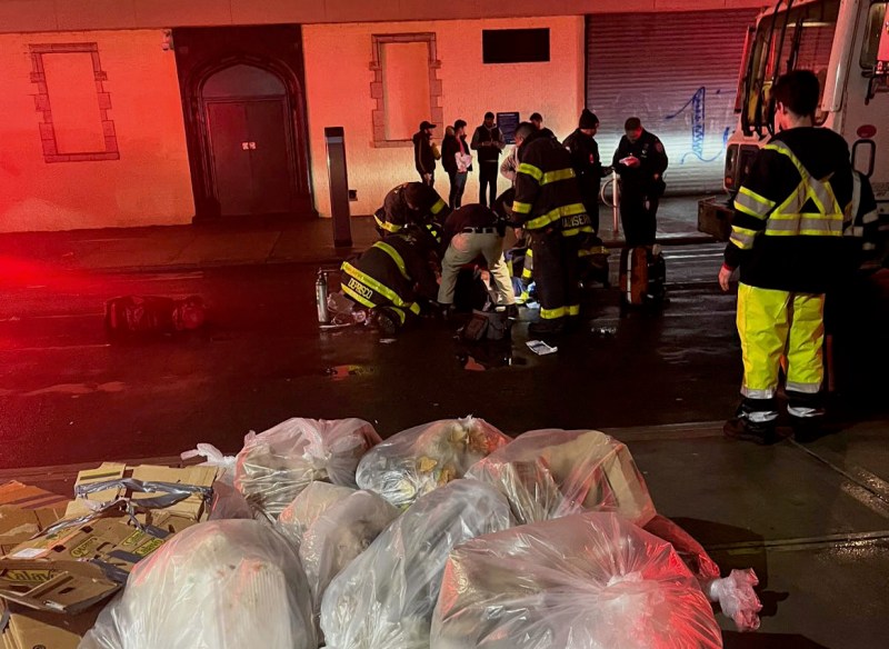 Firefighters work to save the life of Diego Andrade, who was struck by the driver of the garbage truck in the background of the photo.